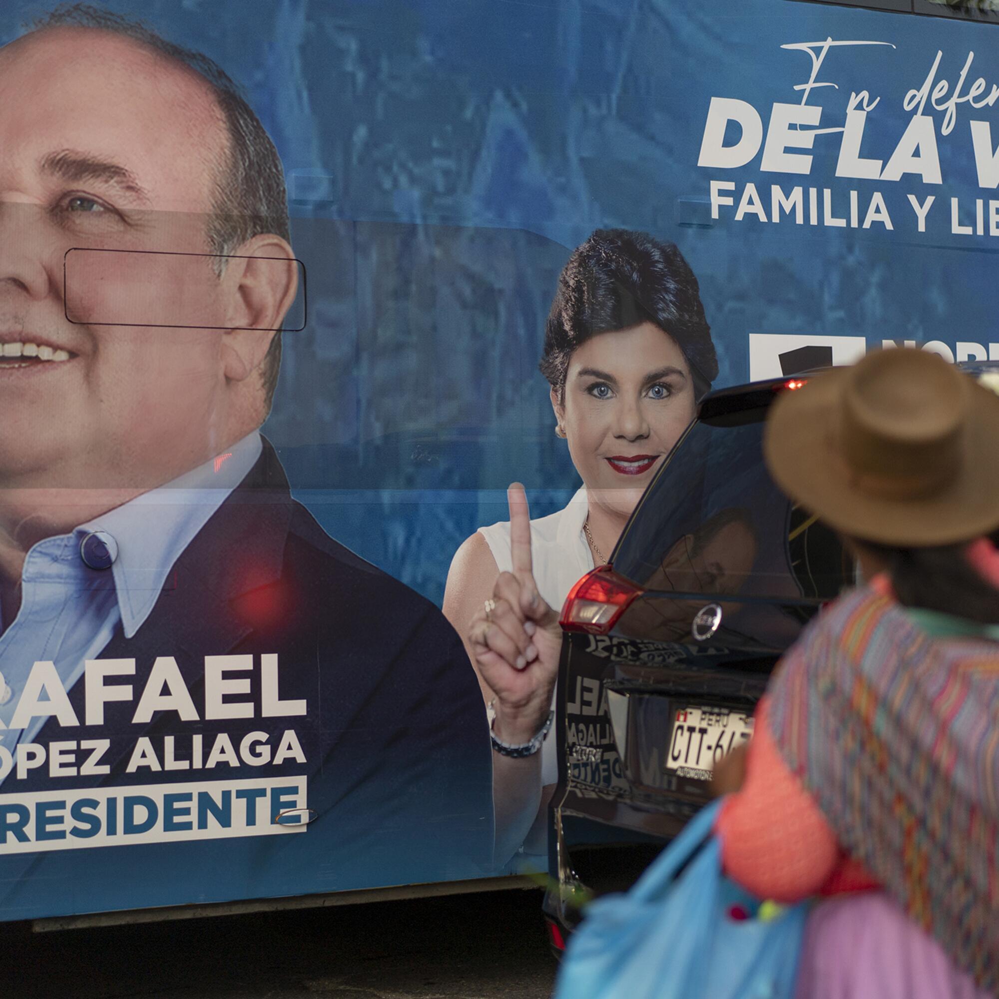 Una mujer con la característica vestimenta de altiplano peruano observa el autobús de propaganda electoral de López Aliaga.