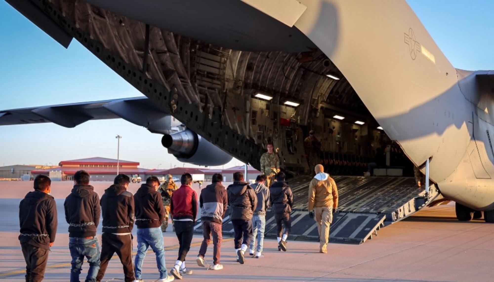 Migrantes esposados entran en un avión militar para su deportación.