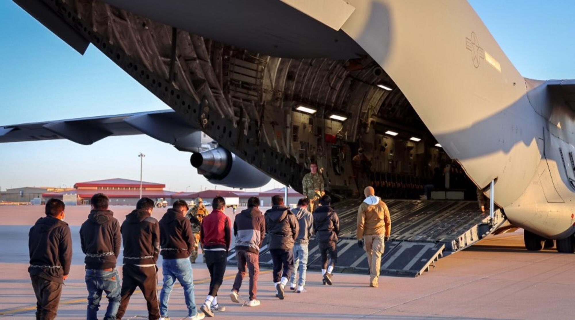 Migrantes esposados entran en un avión militar para su deportación.